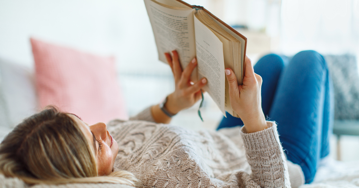 Image: © djile / Adobe Stock Young woman lies on her back in bed reading a book