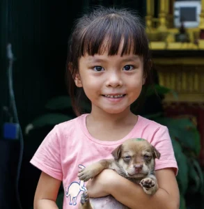 Young Cambodian girl holding a small puppy close to her chest.