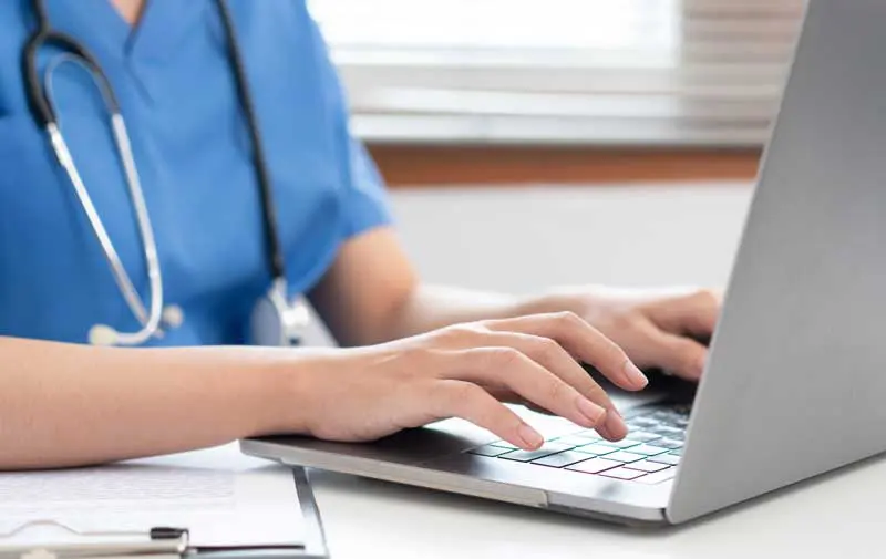 Veterinarian woman in blue uniform is using laptop to searching pet information and typing treatment. Image: Katcha / Adobe Stock